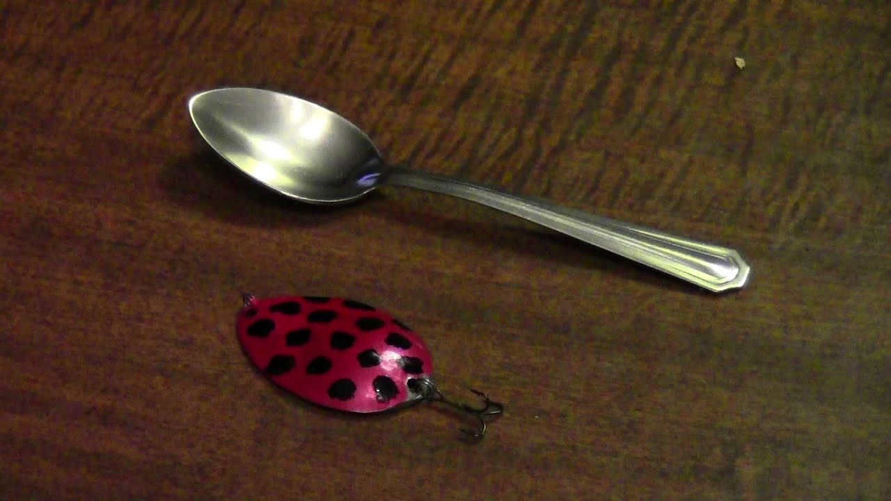 Silver spoon on table with a red black dotted painted spoon end turned into a fishing lure with hook attached