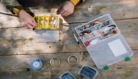 Person organizing Bass fishing baits in plastic tackle organizers on a wooden picnic table